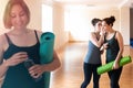 A young woman with a Mat and bottle in her hands. In the background stands two women whispering to each other.The concept of Royalty Free Stock Photo