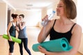 A young woman with a Mat in her hands drinking water from a bottle. In the background stands two women whispering to each other. Royalty Free Stock Photo