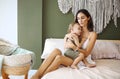 Young woman mother expressing love to little baby, sitting on bed with sleeping child in hands and kissing it in forehead Royalty Free Stock Photo