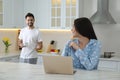 Young woman in pajamas using laptop while boyfriend bringing coffee at home