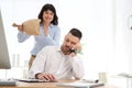 Young woman popping paper bag behind her sleeping colleague. April fool`s day