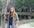 Young women poses outdoors next to a tree and lake