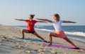 Young women practicing yoga on the beach. Beautiful girls doing yoga standing in Warrior pose Royalty Free Stock Photo