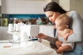 Young woman sews at home and holds a small child. Mom teaches her little son to sew on a sewing machine. Self-isolation Royalty Free Stock Photo