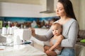 Young woman sews at home and holds a small child. Mom teaches her little son to sew on a sewing machine. Self-isolation Royalty Free Stock Photo