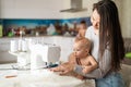 Young woman sews at home and holds a small child. Mom teaches her little son to sew on a sewing machine. Self-isolation Royalty Free Stock Photo