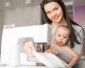 Young woman sews at home and holds a small child. Mom teaches her little son to sew on a sewing machine Royalty Free Stock Photo