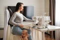 Young woman sews at home and holds a small child. Mom teaches her little son to sew on a sewing machine Royalty Free Stock Photo