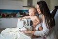 A young woman sews in the kitchen and holds a small child. Mom teaches her little son to sew on a sewing machine. Self Royalty Free Stock Photo