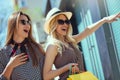 Young women with shopping bags pointing finger to shop window Royalty Free Stock Photo