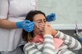 young woman siting in dental clinic on chair having panic attack covering her mouth with both hands