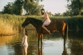 Woman sits astride a horse and other woman bathes in river