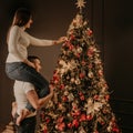 Young woman sits on back shoulders of man and decorates a Christmas tree Royalty Free Stock Photo