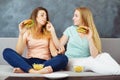 Young women sitting at coach eating burgers Royalty Free Stock Photo