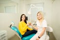 Young woman sitting in dental chair with female dentist, showing fresh apples after successful dental treatment