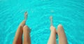 Young women sitting on edge of pool and dangling their feet in water. Two girls with slim tanned legs relaxing near