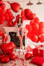 Young woman standing in room filled with mix of red balloons. Girl holding glass of champagne Royalty Free Stock Photo