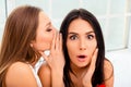 Young woman telling secrecy news to her surprised girlfriend