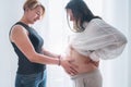 Young woman tender touching partner's female pregnant belly. Same-sex marriage couple next to living room window. health