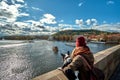 Young women tourist with a puppy dog and a backpack looking at the tourist boat and swans sailing on Vltava river Royalty Free Stock Photo