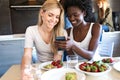 Young women watching her mobile phone while having lunch with friends at home.