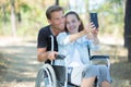 Young woman in wheelchair and boyriend taking selfie outdoors Royalty Free Stock Photo