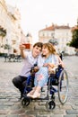 Young woman in wheelchair and her husband taking selfie outdoors, walking in old city center Royalty Free Stock Photo
