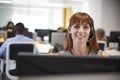 Young woman working at computer with headset in busy office Royalty Free Stock Photo