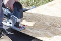 A young worker cuts a sheet of plywood with an electric jigsaw on the street. Royalty Free Stock Photo