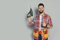 Young worker with power drill and tool belt on grey background. Space for text Royalty Free Stock Photo