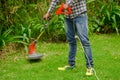 Young worker wearing jeans and long sleeve shirt and using a lawn trimmer mower cutting grass in a blurred nature Royalty Free Stock Photo