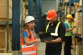 Young workers are checking order details on a tablet while standing between retail warehouse full of shelves