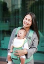 Young working mother carrying her infant by ergonomic baby carrier Royalty Free Stock Photo