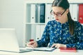 Young woman using laptop and reading annual report document at work. Business woman working at her desk.