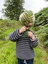 A young 2 year old boy hiding behind a fern leaf playing outdoors