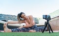 Young yoga teacher recording an online class with her mobile phone in the garden of her house. She is doing leg stretching