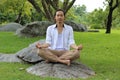 Young yogi man doing yoga meditation while sitting in lotus position on the rock in the park. Royalty Free Stock Photo