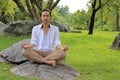 Young yogi man doing yoga meditation while sitting in lotus position on the rock in the park. Royalty Free Stock Photo