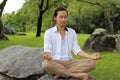 Young yogi man doing yoga meditation while sitting in lotus position on the rock in the park. Royalty Free Stock Photo
