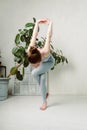 Young yogini practicing in a room with white walls and plant