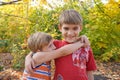 The younger brother hugs the older one and looks at him, two loving brothers are standing in an embrace in the park against the Royalty Free Stock Photo