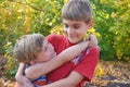 The younger brother hugs the older one and looks at him, two loving brothers are standing in an embrace in the park against the Royalty Free Stock Photo