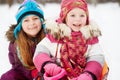 Younger girl sits in sled, older one sits behind her