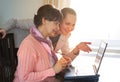 Younger woman helping an elderly person using laptop computer for internet search. Young and pension age generations working Royalty Free Stock Photo