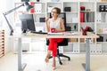 A young girl is sitting at a table in the office, holding a pencil and a red cup in her hands. Royalty Free Stock Photo