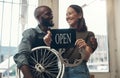 Your bike is in good hands here. Shot of a young couple standing together in their bicycle shop and holding an open sign Royalty Free Stock Photo