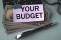 YOUR BUDGET - words on a white piece of paper fixed on banknotes against the background of a calculator, glasses and pen