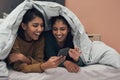 Your crush liked your picture. two young women looking at something on a cellphone while lying on a bed. Royalty Free Stock Photo
