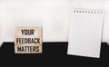 YOUR FEEDBACK MATTERS text on wooden blocks and white and black background with notepad for writing.Business concept Royalty Free Stock Photo