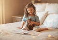 Your imagination has no limits. an adorable little girl at home reading a storybook on her bed with her teddybear.